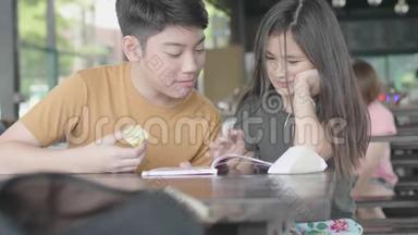 亚洲男孩和女孩用<strong>卡通书</strong>放松，可爱的亚洲孩子坐在咖啡馆里享受读书，微笑着面对